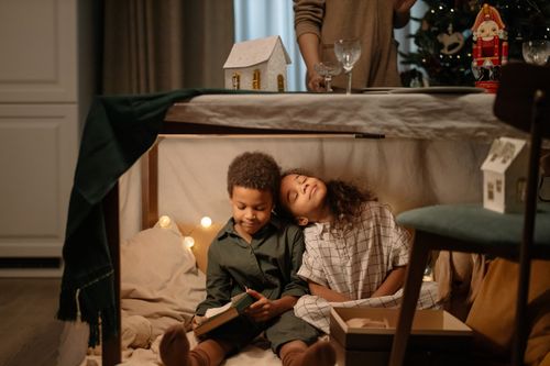 Free Two children sitting under a table enjoying a Christmas scene with cozy decorations. Stock Photo