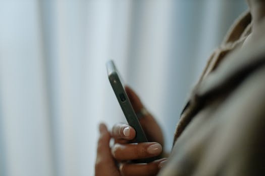 A focused close-up of a female hand holding a smartphone indoors with a soft background.