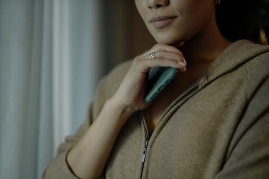 A contemplative woman holds a smartphone while indoors, reflecting a calm mood.