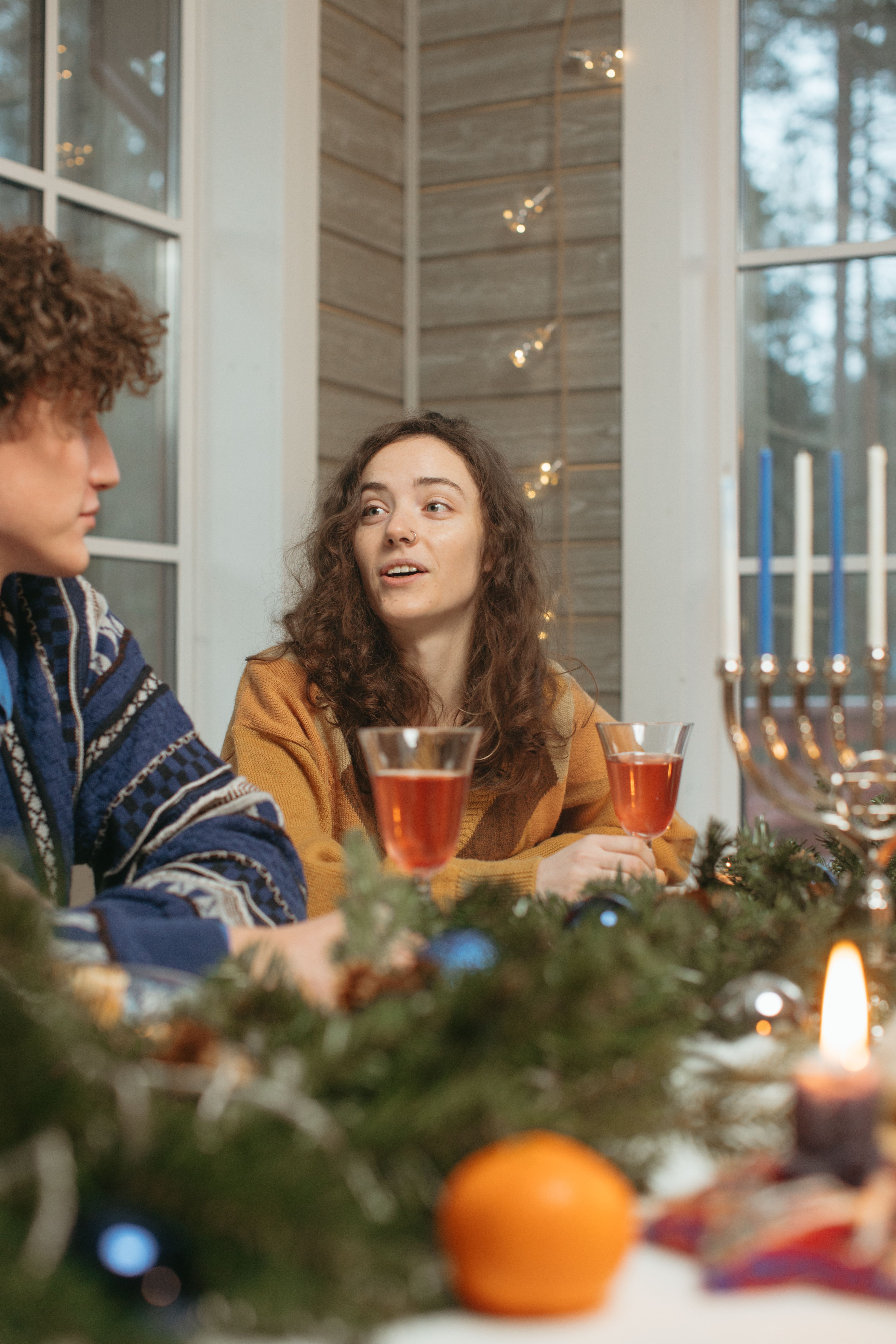 Two friends enjoying a festive Hanukkah celebration indoors with candles and decorations.