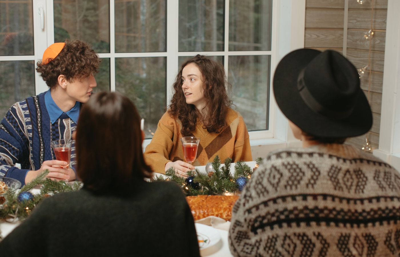 Friends gather indoors around a festive table, enjoying food and conversation during a holiday celebration.