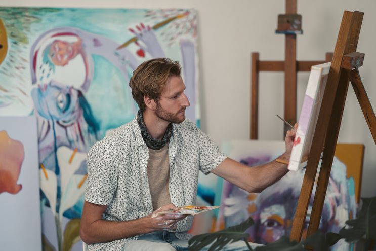 An artist holding a color palette and painting on a canvas in a studio, representing the primary talent expressing as a visible, usable gift