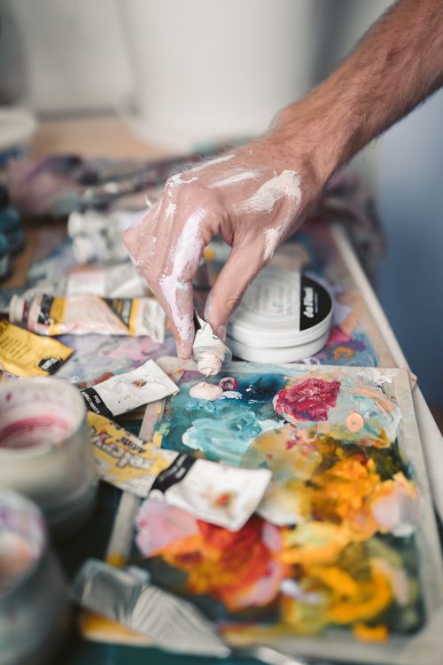 Free Close-up of hand mixing oil paints on a palette with paint tubes and brushes around. Stock Photo