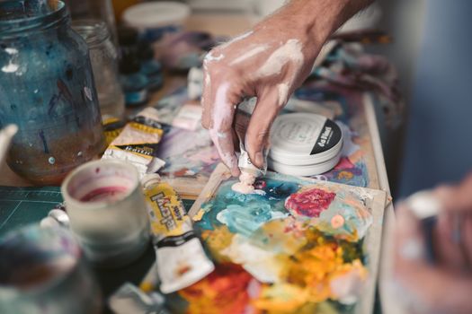 A detailed view of an artist's hand mixing vivid oil paints with a palette knife.