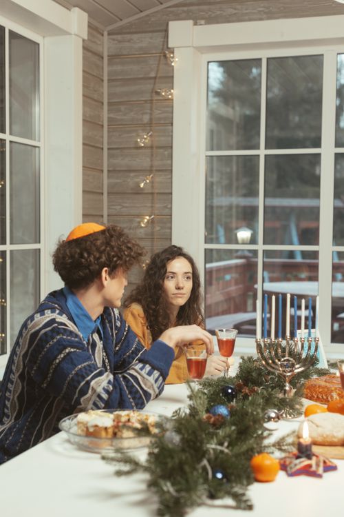 Free A man and woman enjoy Hanukkah dinner beside a menorah and festive decor. Stock Photo