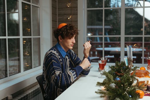 Man in blue sweater celebrating Hanukkah with menorah and wine indoors.