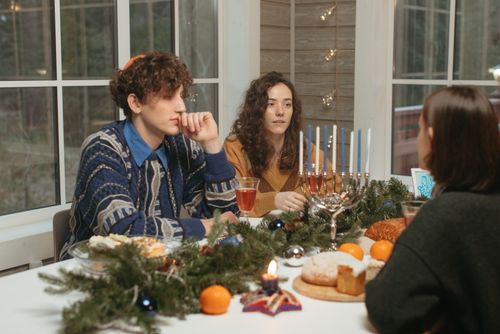 Free Friends gather at a winter dinner table to celebrate Hanukkah with menorah and festive food. Stock Photo
