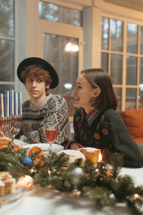Free A warm and festive Hanukkah gathering with menorah, food, and happy friends in cozy sweaters. Stock Photo