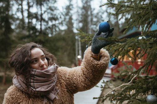 Free Woman placing a blue bauble on a Christmas tree outdoors in winter. Stock Photo