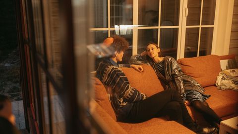 Two adults having a relaxed conversation on a sofa in a warm indoor setting.