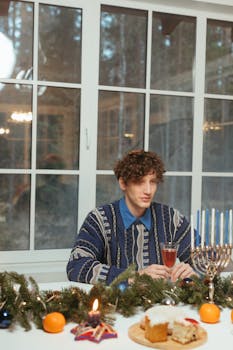 Man enjoying a Hanukkah celebration with menorah, candles, and traditional food.