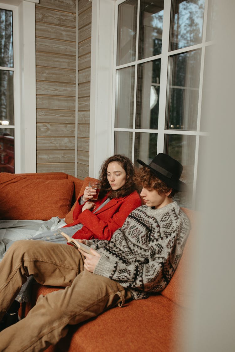 Man Wearing A Gray Sweater Sitting On The Couch Reading A Book