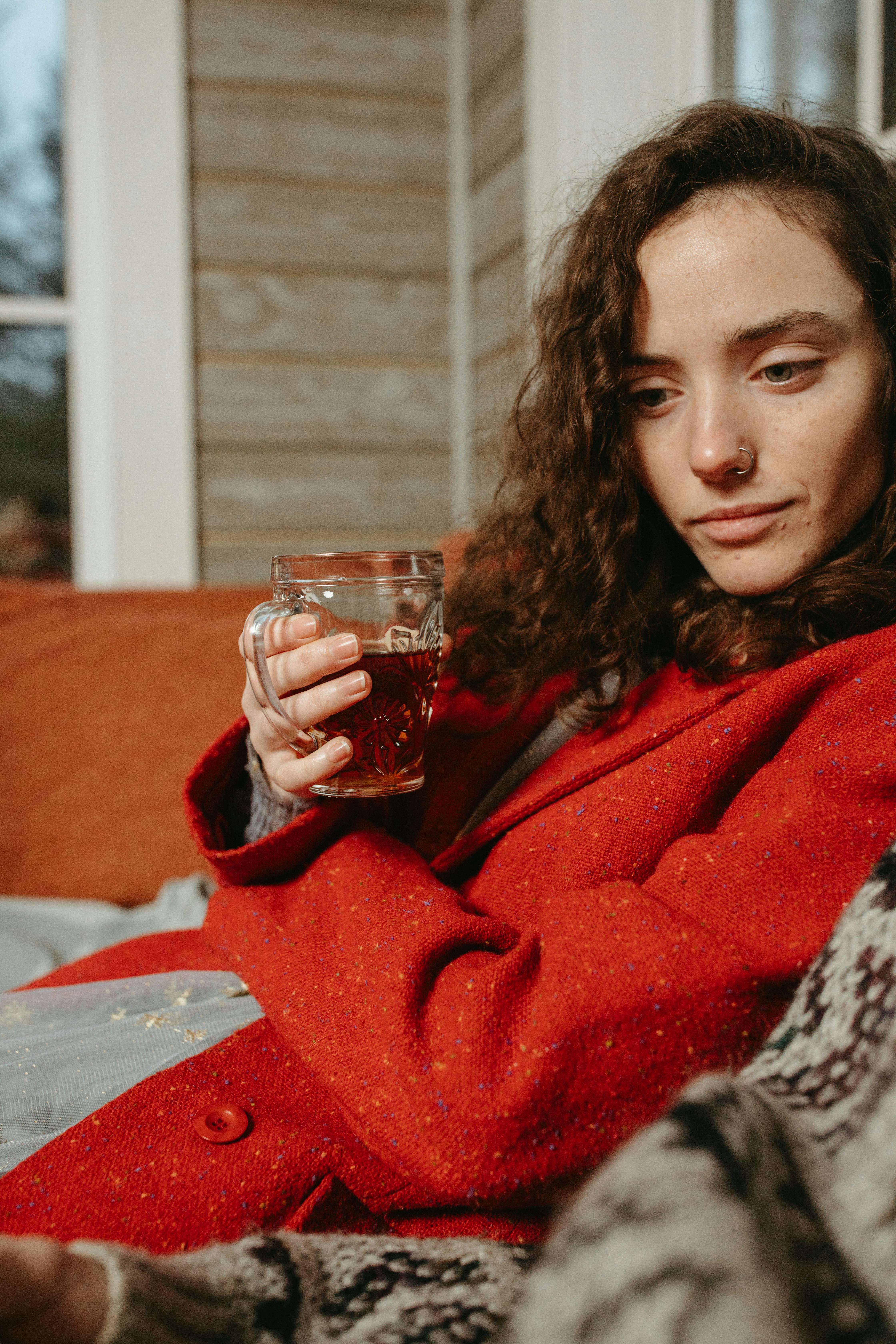 穿着红色外套的女人拿着饮料，在舒适的沙发上放松