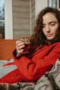 穿着红色外套的女人拿着饮料，在舒适的沙发上放松