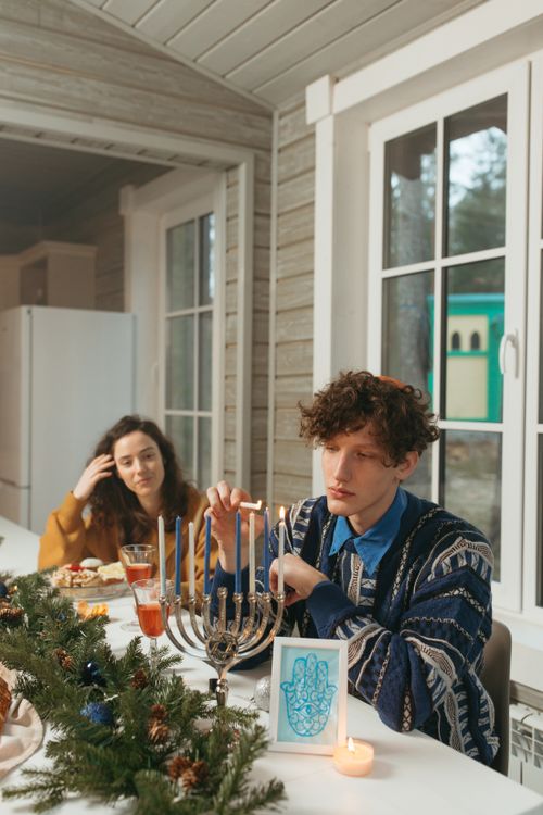 Free Two friends celebrating Hanukkah with a menorah, candles, and festive table setting. Stock Photo