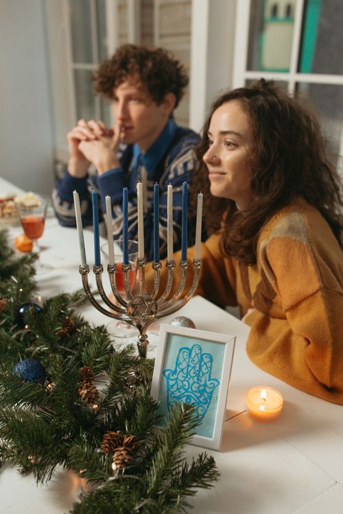 Free Two people enjoying a Hanukkah celebration with a lit menorah and festive decor. Stock Photo