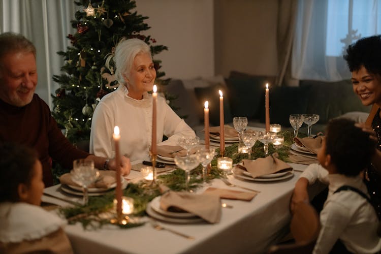 An Elderly Woman Smiling At A Dining Table With Her Family