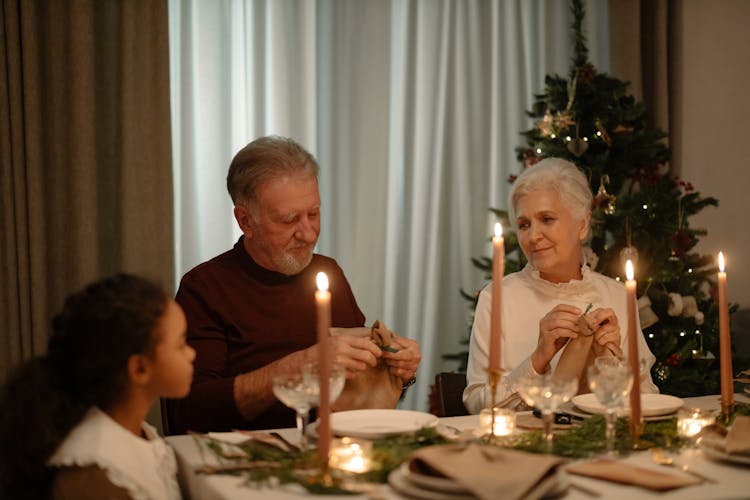 An Elderly Man And Woman Sitting At A Dining Table On Christmas