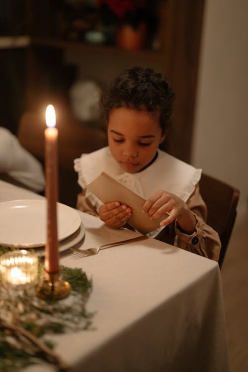 A Kid Sitting at a Dining Table Opening an Envelope