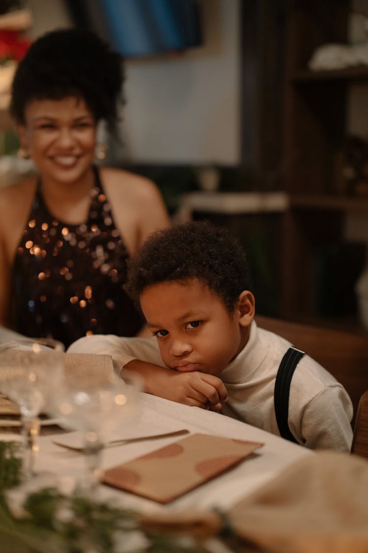 A Kid Sitting At A Dining Table Pouting