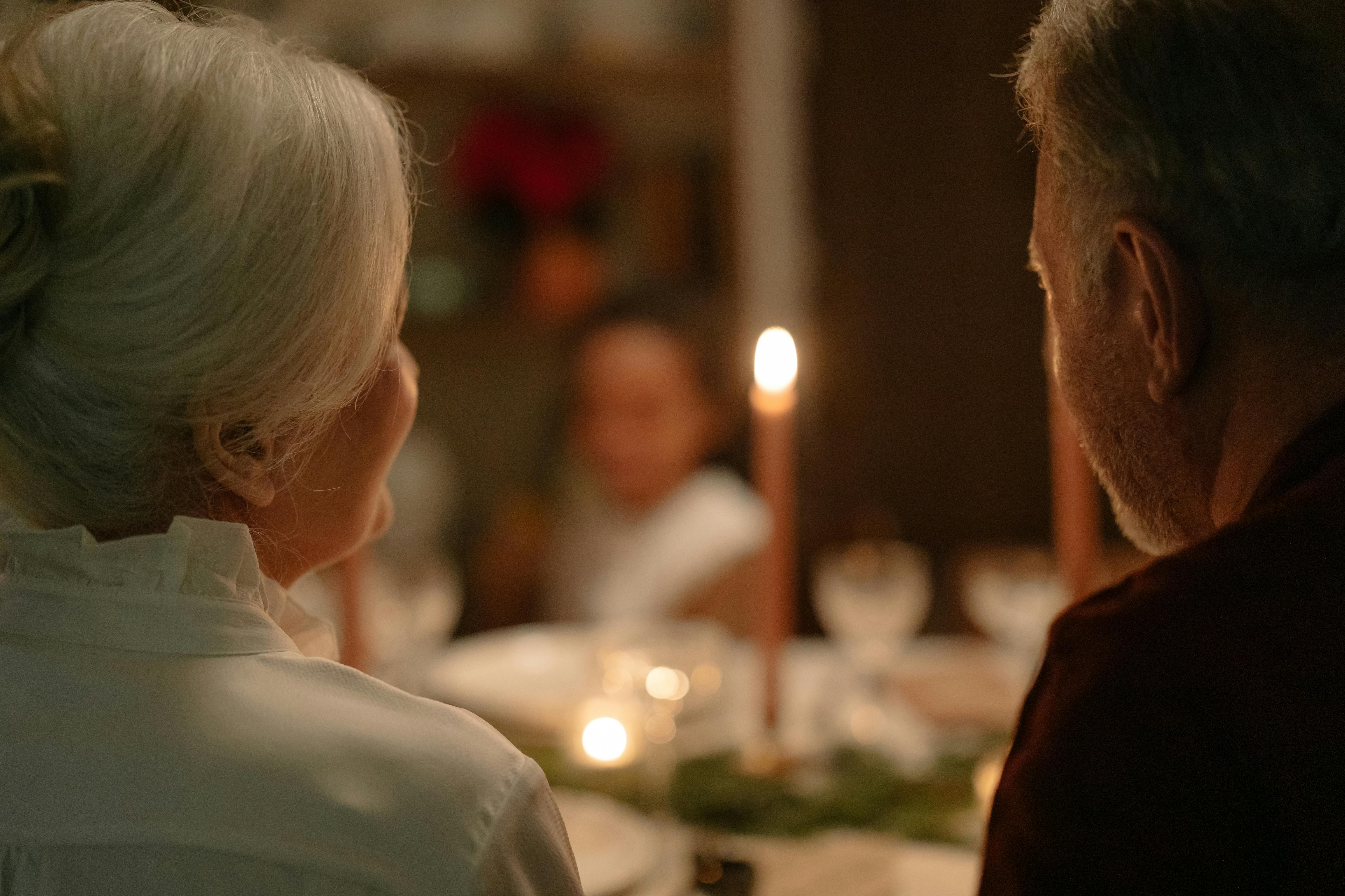 Elderly couple sharing a warm, intimate candlelit dinner at home.