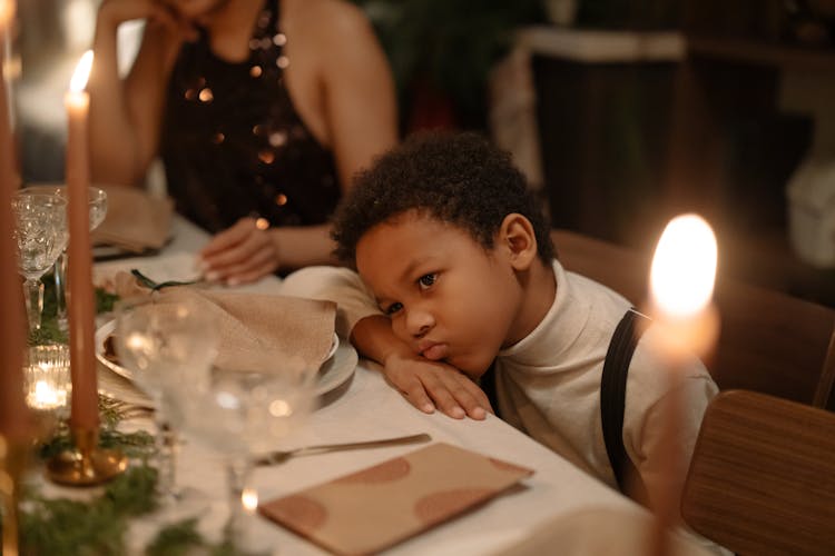 A Kid Sitting At A Dining Table Pouting