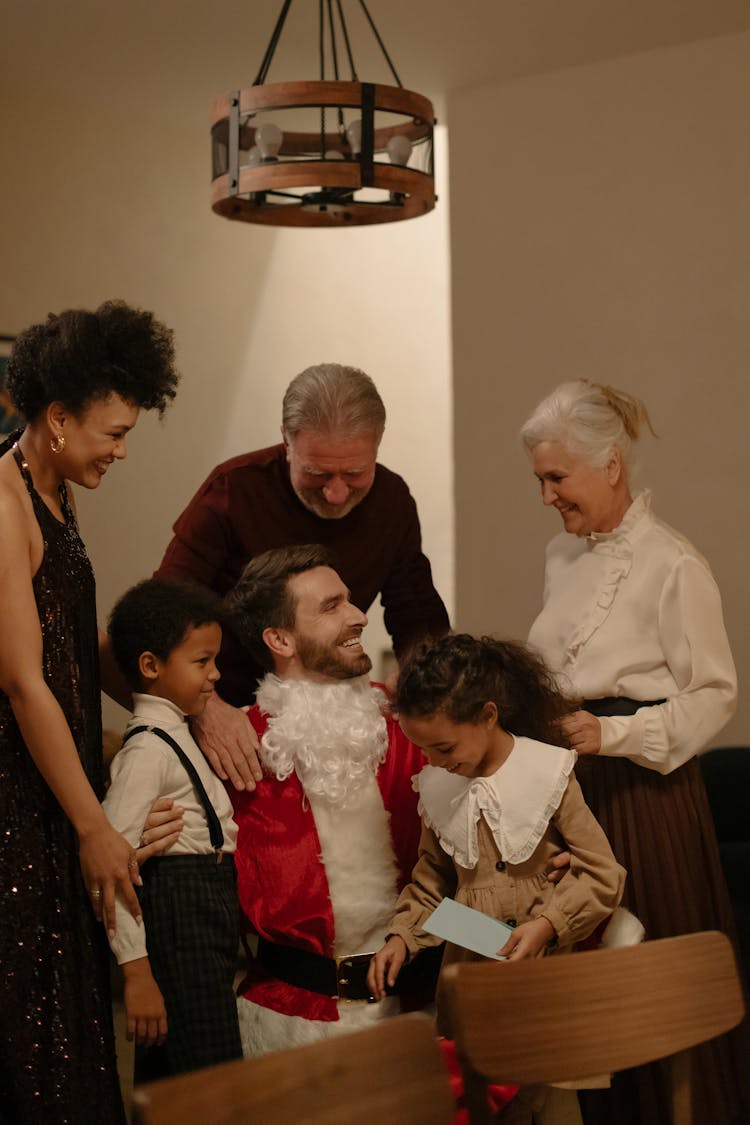 A Man Wearing A Santa Claus Costume At A Family Gathering