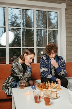 Two young adults focus intently while playing chess on a cozy afternoon indoors.