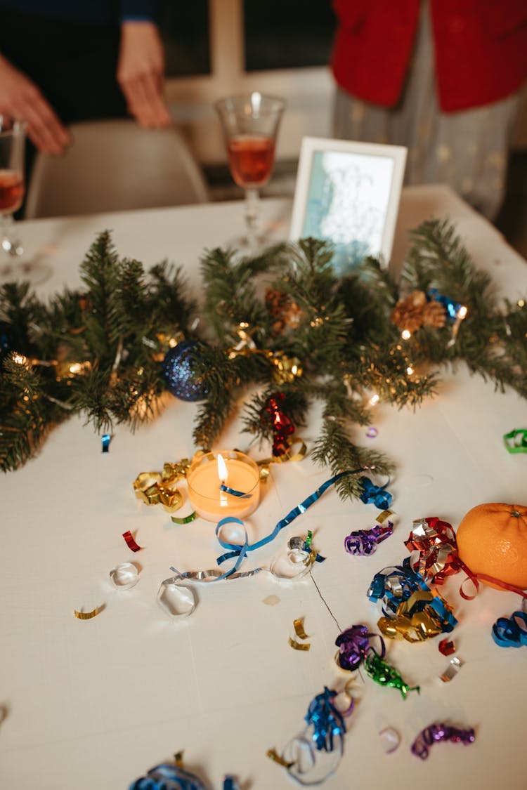 Christmas Baubles On White Table Beside A Lighted Candle