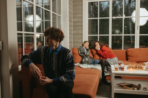 Man in Blue and Black Sweater Sitting on Orange Couch