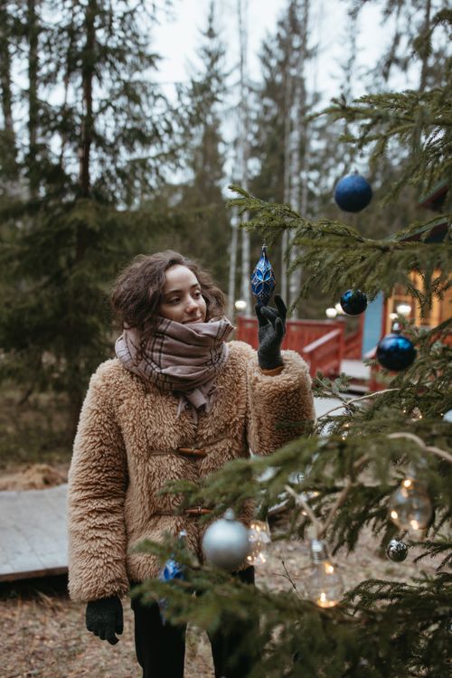 Free Woman in fur coat adorning a Christmas tree with ornaments during winter outdoors. Stock Photo