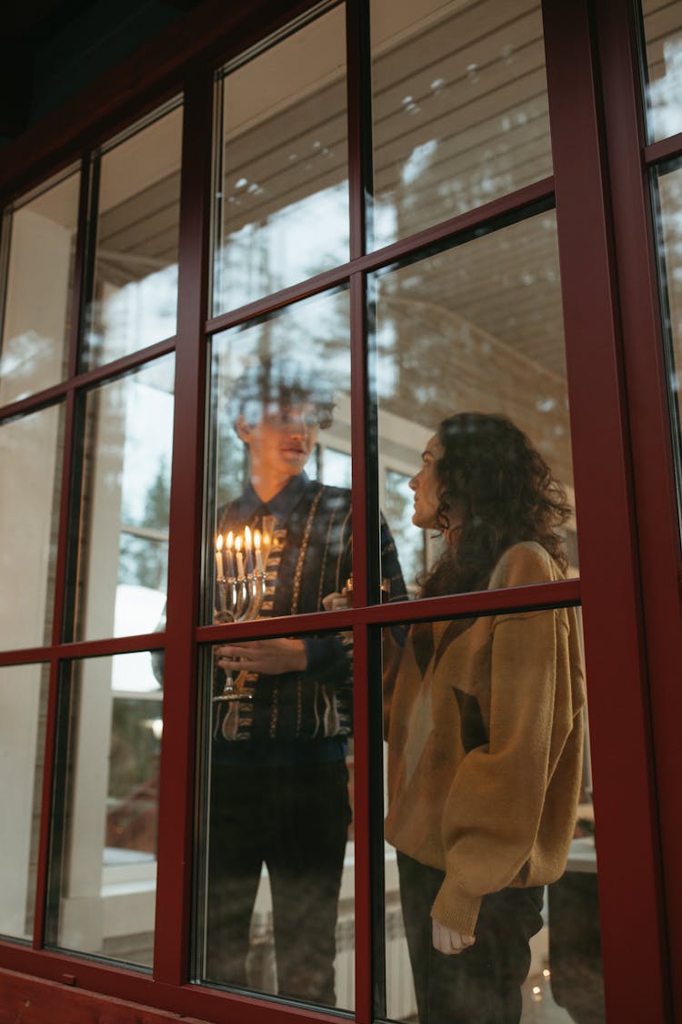 Man Holding A Menorah Standing Near The Window