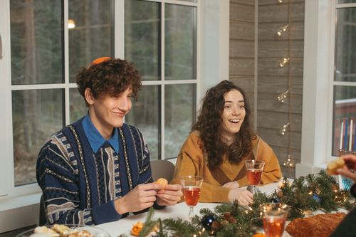 Free A cozy holiday dinner with friends enjoying festive lights and warm drinks indoors. Stock Photo