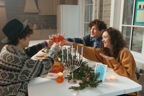 Free Friends enjoy a cozy Hanukkah dinner with candles, food, and drinks, celebrating together indoors. Stock Photo