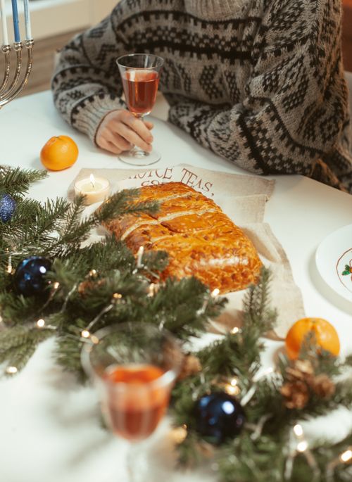Free Cozy holiday dining setting with bread, decorations, and a person holding a drink. Stock Photo