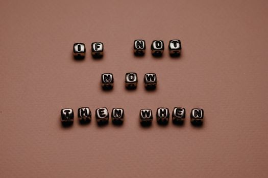 Metal letter cubes spelling 'If not now, then when' on a beige surface, promoting motivation.