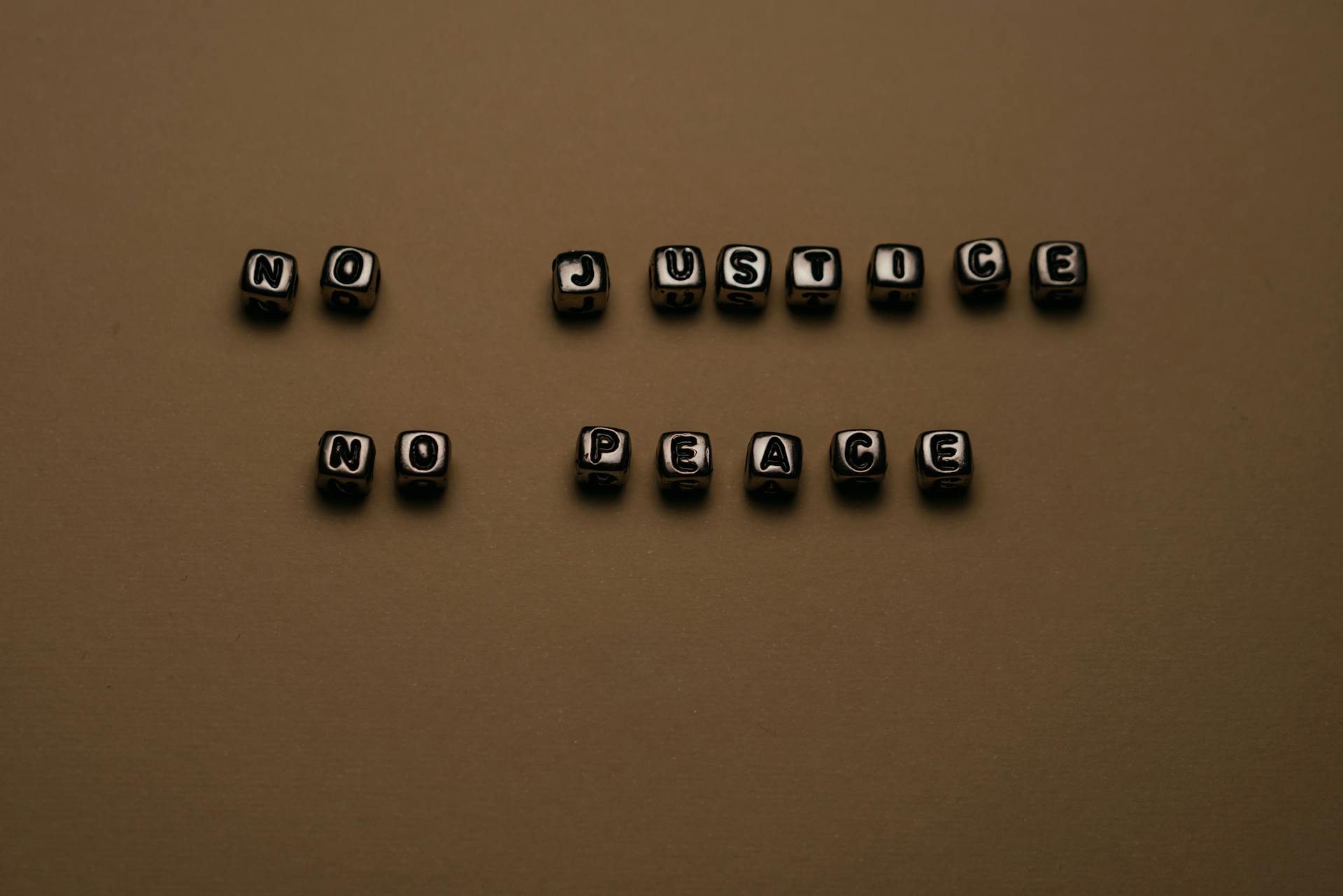 Letter blocks spelling 'No Justice No Peace' on brown background, highlighting social justice themes.