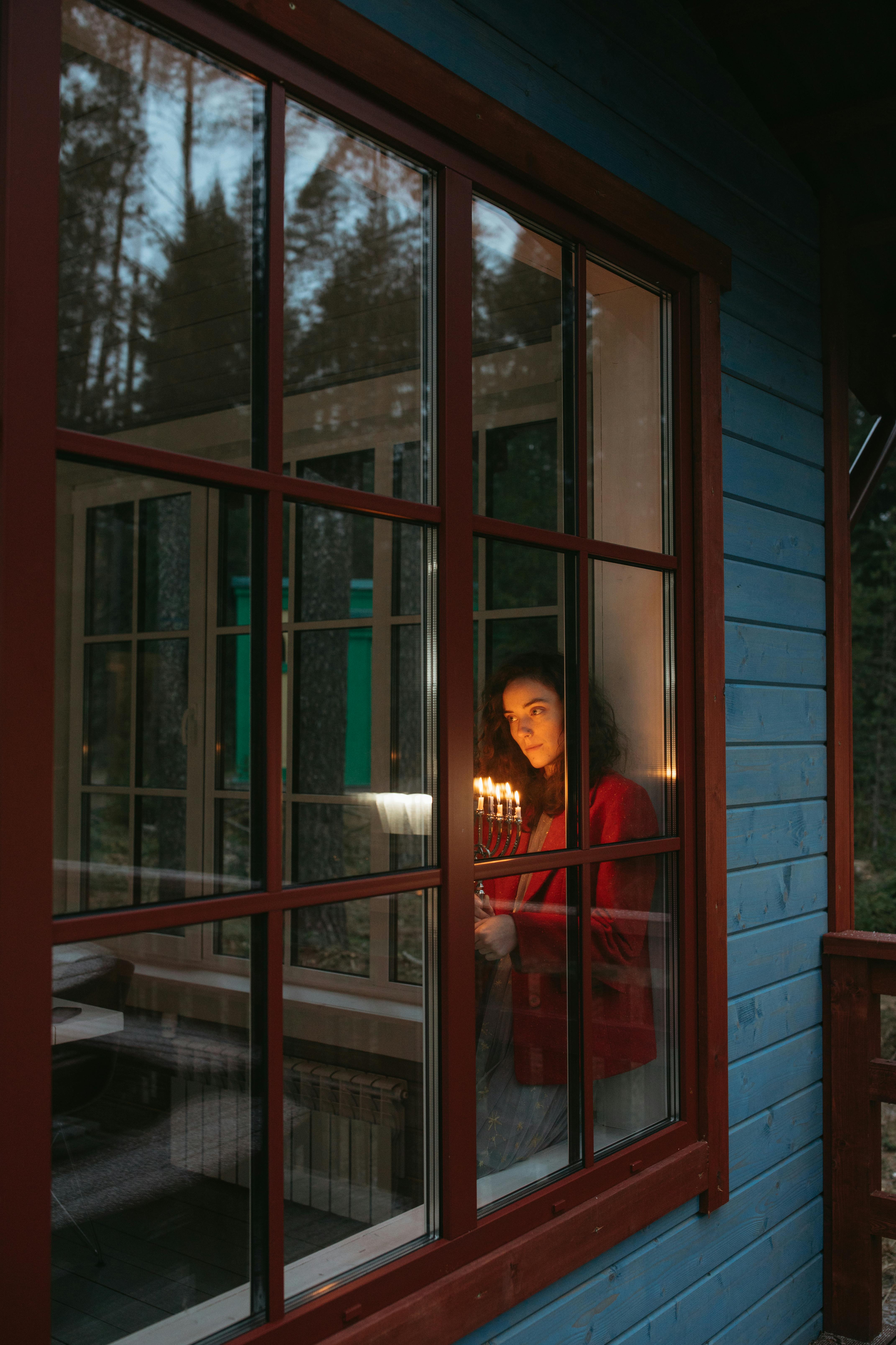 A woman stands by a window holding a menorah lit with candles, celebrating Hanukkah.