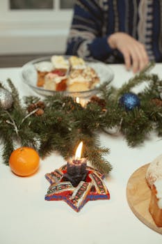 A cozy holiday setting featuring a candle, desserts, and festive greenery.