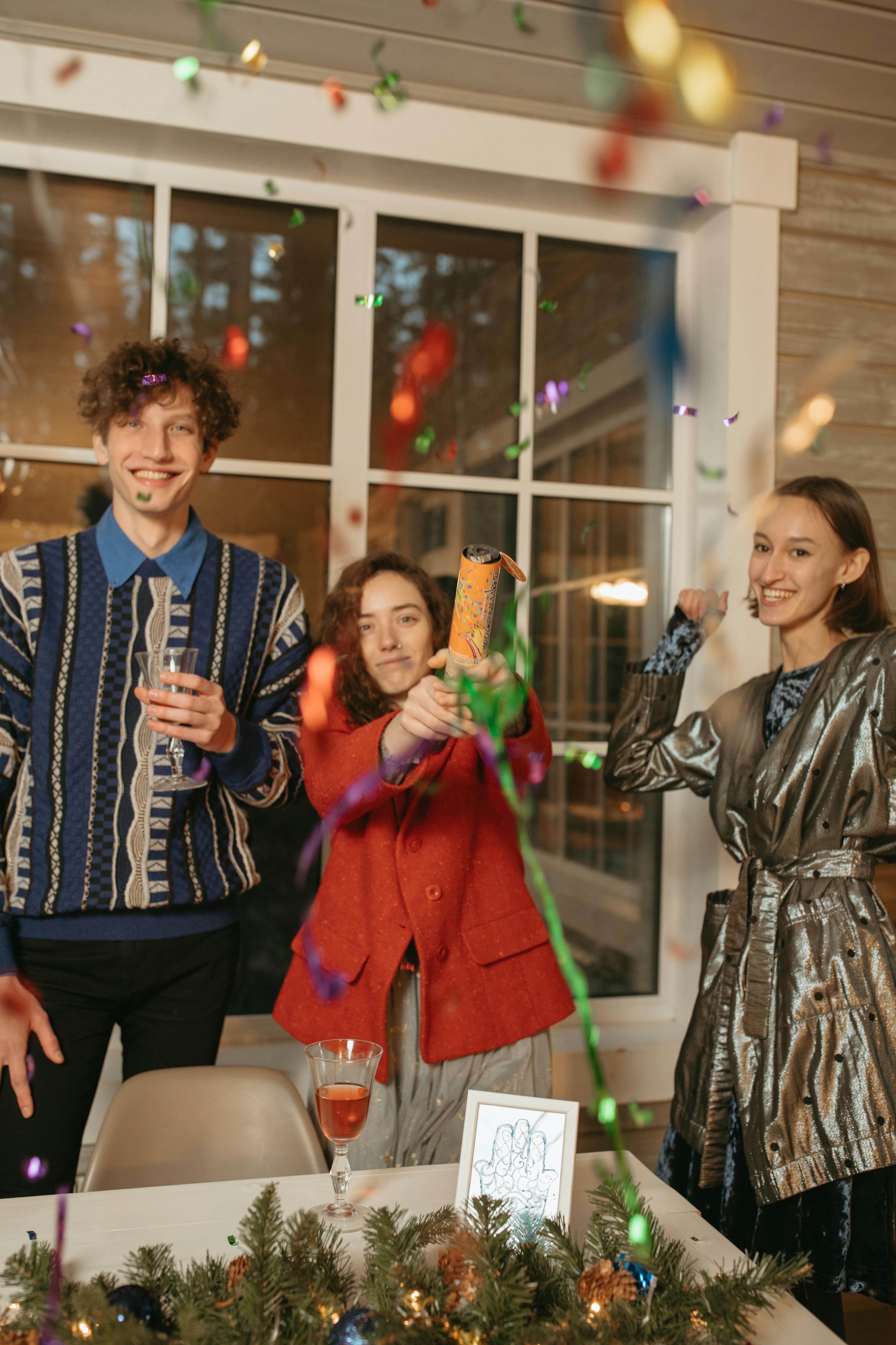 Three friends joyfully celebrating with confetti indoors during a festive event.