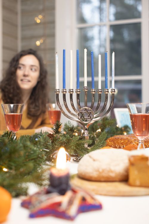Free A woman enjoys a festive Hanukkah meal with a menorah centerpiece and holiday decor. Stock Photo