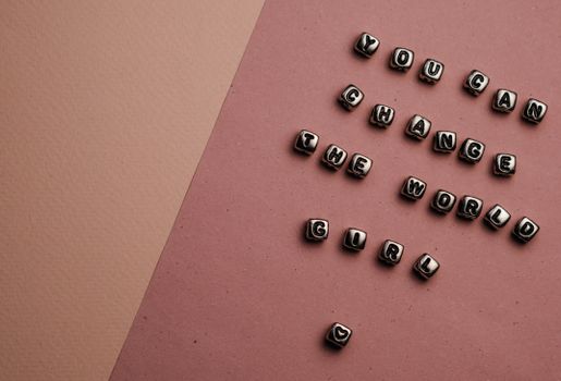 Beaded letter cubes on pink background spell out feminist message: You Can Change the World Girl.