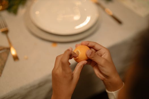 Close-up of hands peeling a lemon on a table with ceramic plates, creating a cozy dining atmosphere.