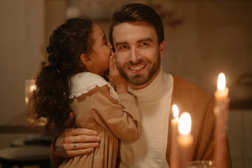 Free A father and daughter share a secret in warm candlelight, capturing a moment of love and bonding. Stock Photo