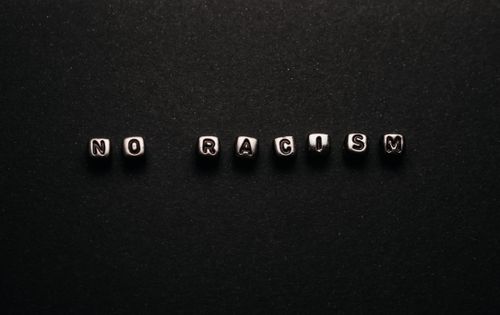 Free Close-up of 'NO RACISM' spelled out with beads on a dark background, promoting social awareness. Stock Photo