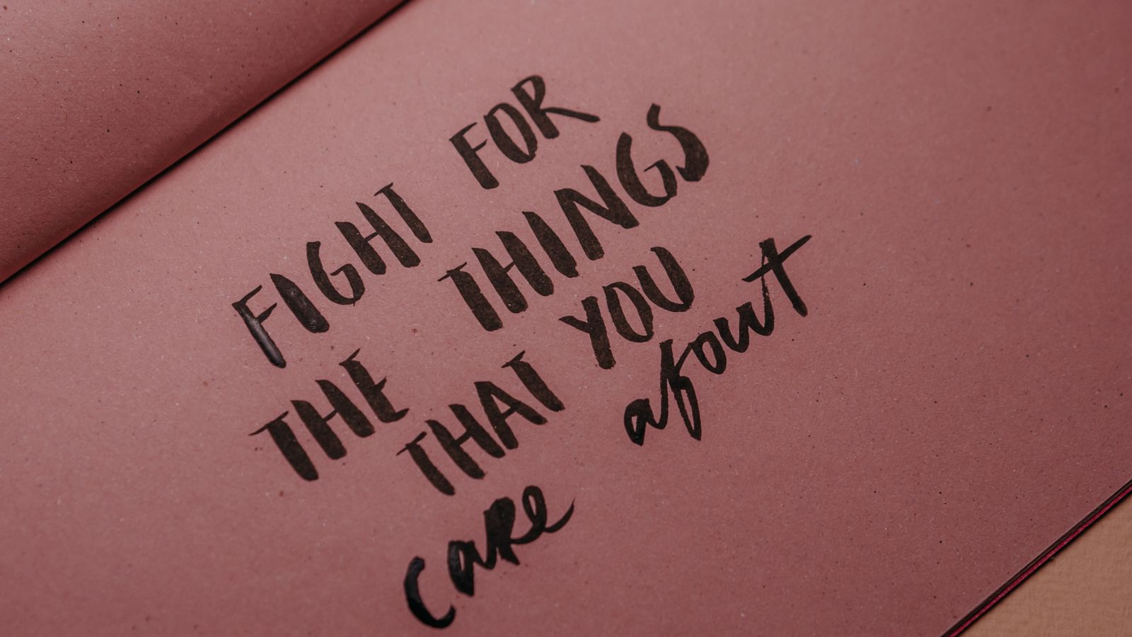 A handwritten motivational quote on pink notebook paper reading “Fight for the things that you care about”