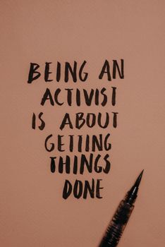 Inspirational calligraphy message about activism with a calligraphy pen on brown paper.