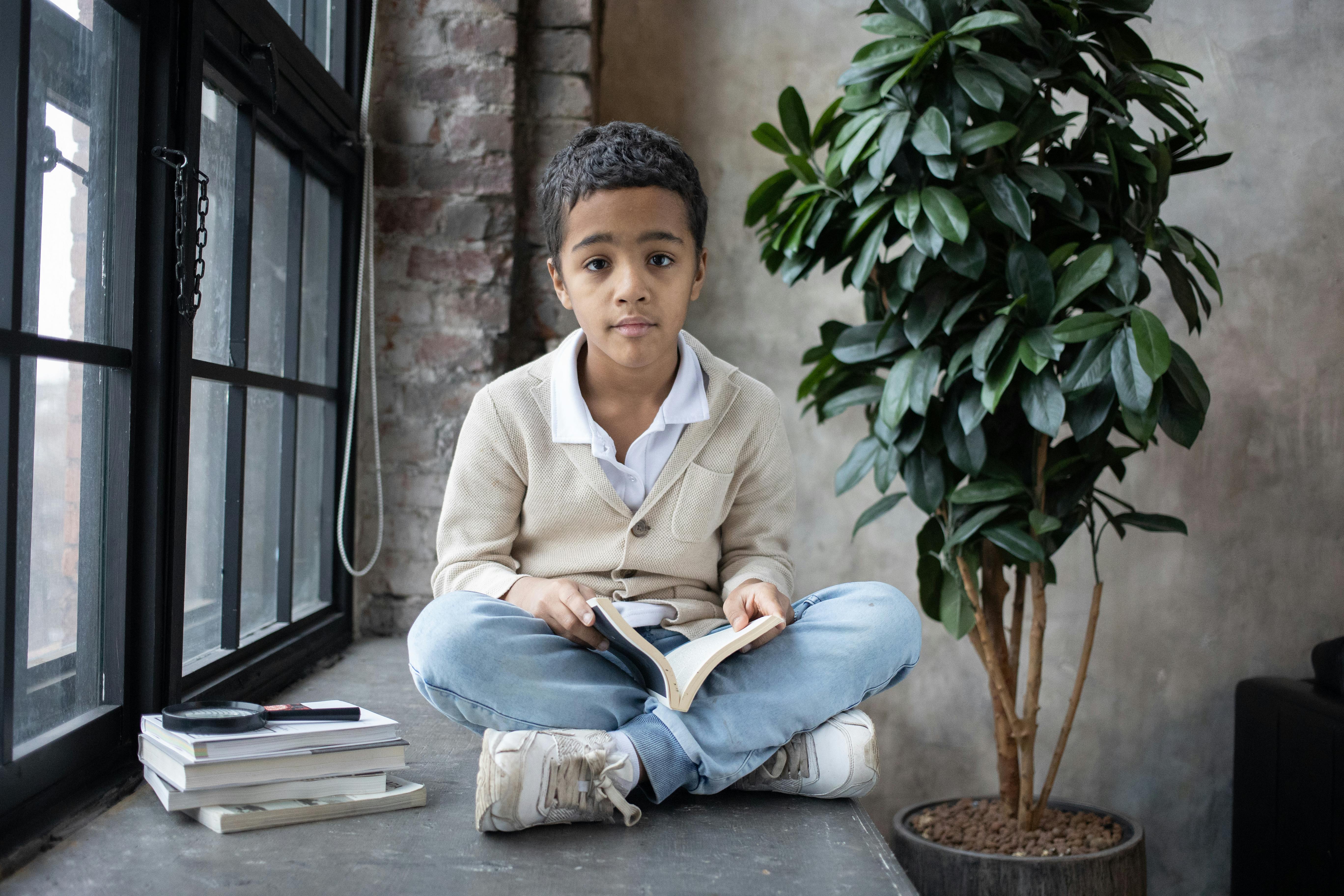 adorable arabian boy sitting on windowsill with opened book on knees