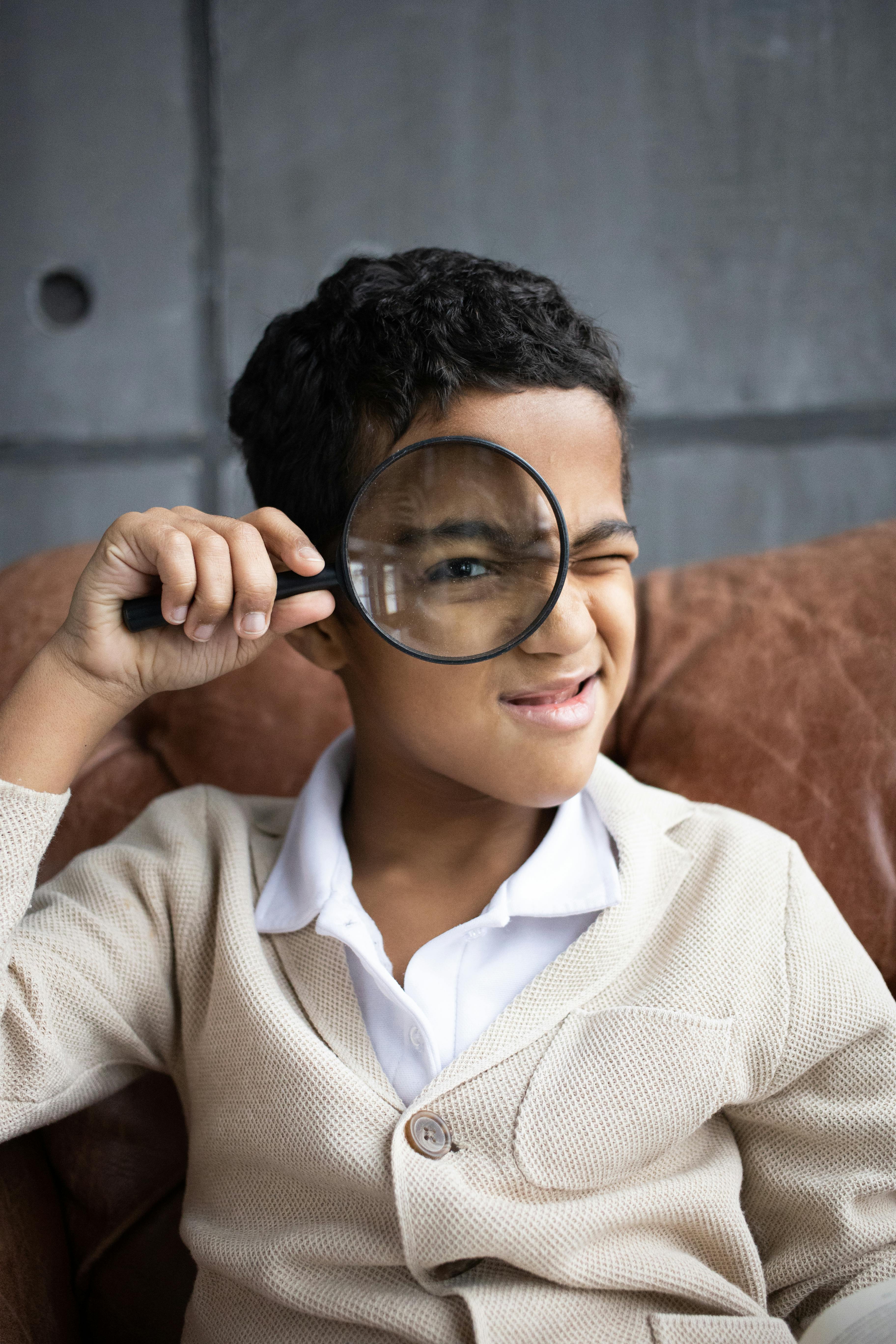 curious schoolboy looking through magnifier at camera in room