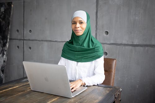 Positive Arab female freelancer using laptop while sitting at table